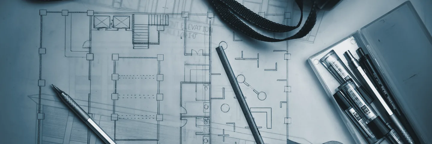Floor-plan drawings on a desk with drafting pencils and a metal ruler.